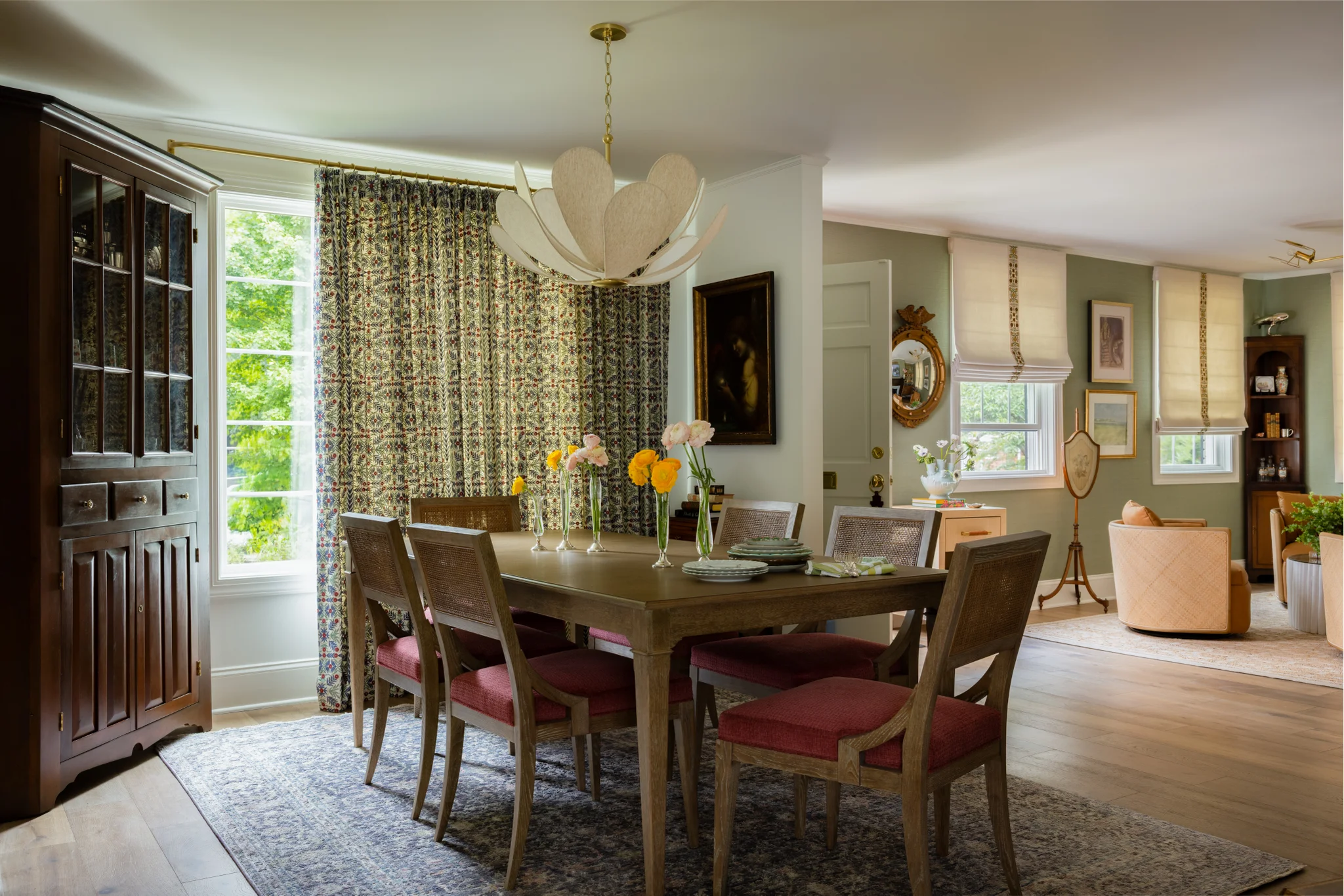 Dining room with a wood dining table, red upholstered chairs, patterned curtains, and a white chandelier