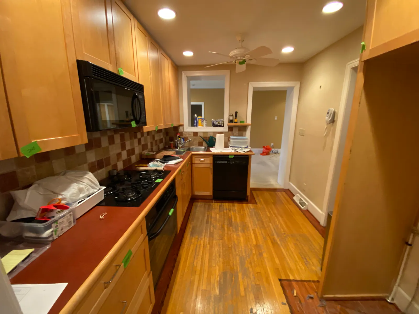 Before whole-home remodel in Sedgefield, galley kitchen with wood cabinets, brown tile backsplash, and wood floor