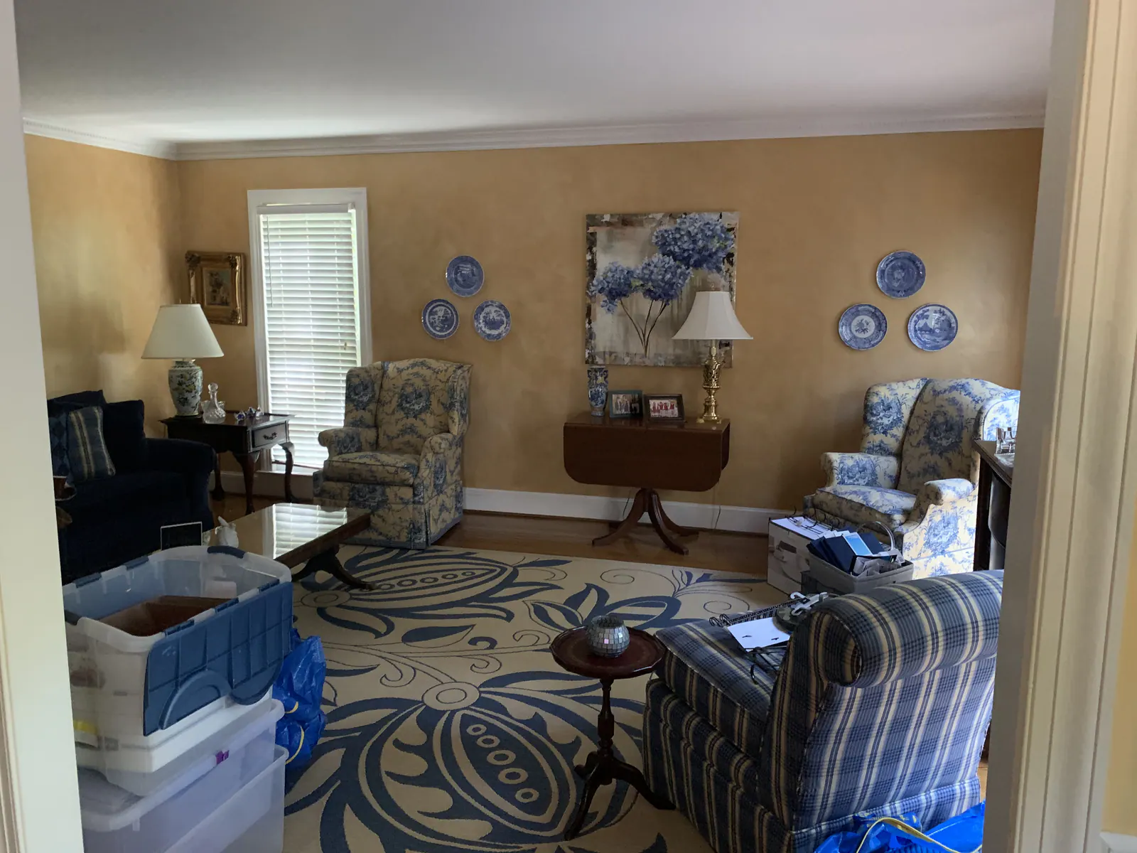 Living room with gold walls, blue and white patterned rug, and blue upholstered furniture