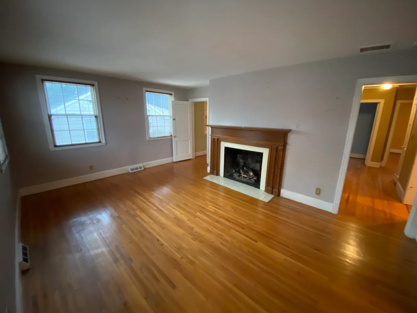 Before: Sedgefield living room with light gray walls, hardwood floors, and a wood fireplace mantel